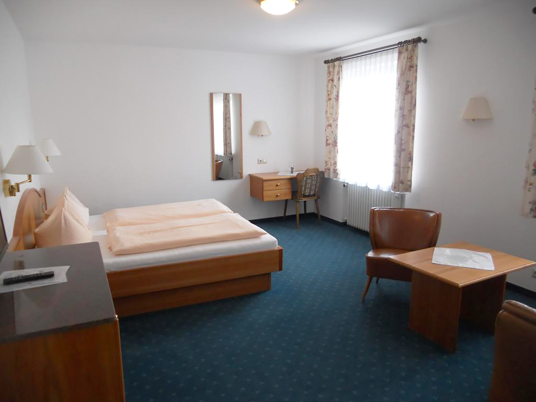 Doppelzimmer mit großem Doppelbett, Nachttischen mit Lampen, Sitzbank und Fenster mit Blick ins Grüne
