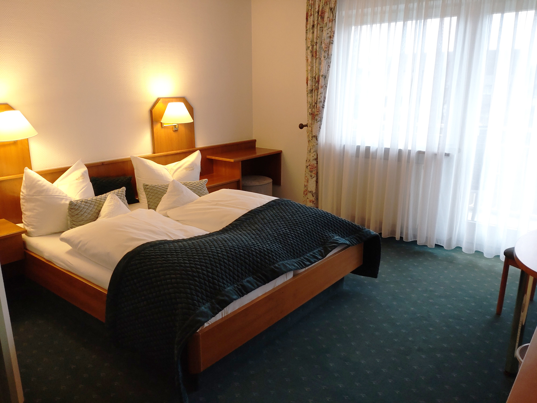 Ost-Doppelzimmer mit Doppelbett, Holzboden, Nachttischlampe und Blick auf grüne Wiese