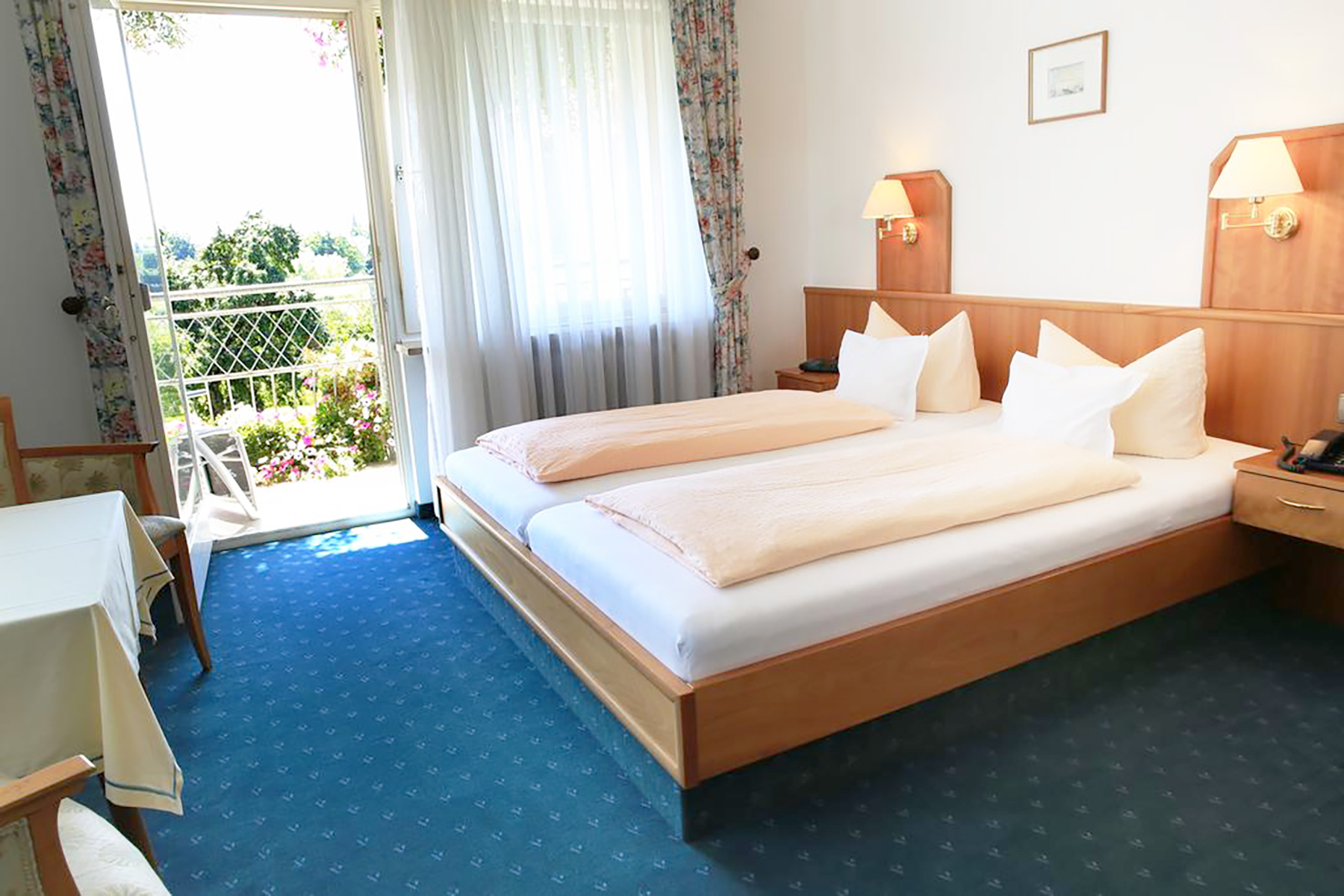 Ost-Doppelzimmer mit Doppelbett, Holzfußboden, Nachttisch und Fenster mit Blick auf grüne Wiese