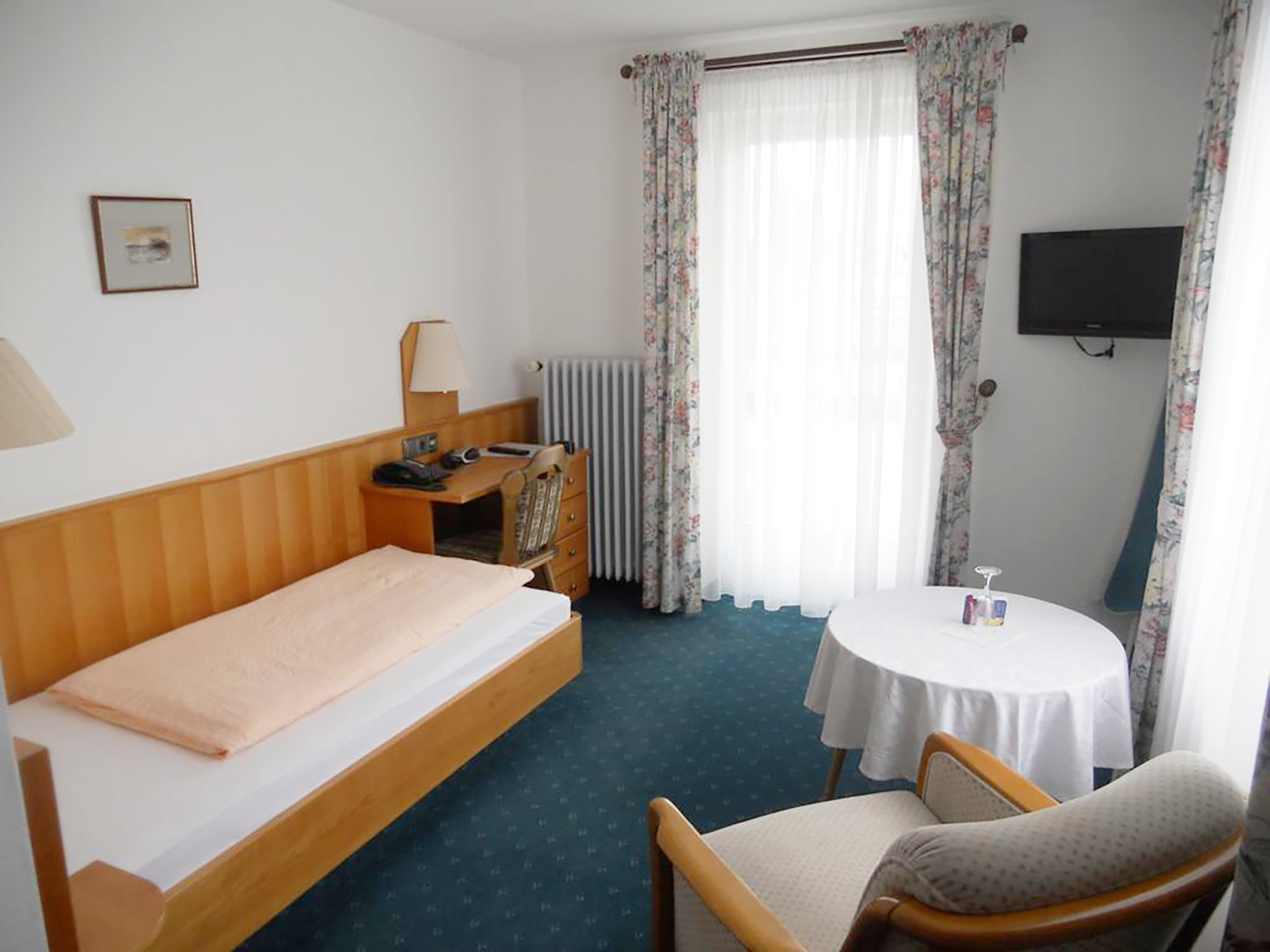 Einzelzimmer mit Einzelbett, Holzboden, Nachttischlampe und Fensterblick ins Grüne
